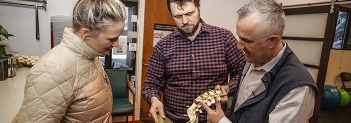 Chiropractor Anchorage AK Kelly Ryan And Christian Langford Pointing To Spine Model With Patient